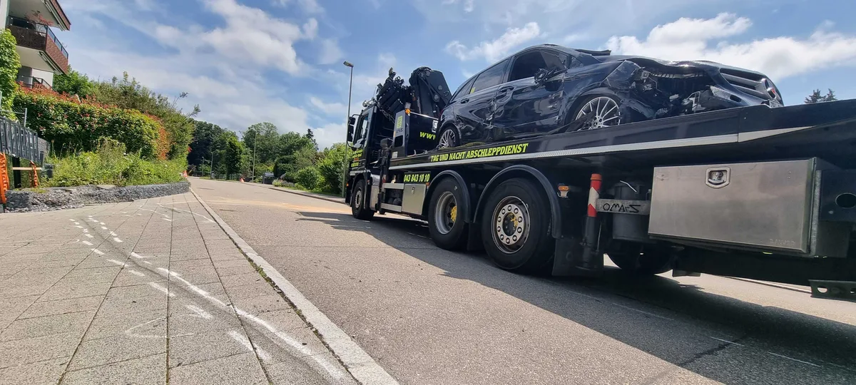 Hier dürfte der dunkle Mercedes ein zweites Mal mit einem niedrigen Schottersteinmäuerchen kollidiert sein. Man sieht eine Unfallstelle und ein stark beschädigtes Unfallauto.